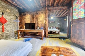 A rustic room with a wooden ceiling, a stone wall, a wooden table, a bed, and a colorful geometric wall decoration.