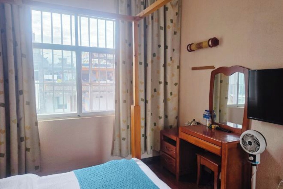 A hotel room with a bed, a desk, a mirror, a TV, and a window with curtains.