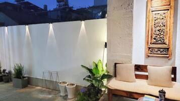 A patio area with a cushioned seating arrangement, a small table, and a decorative wall piece.