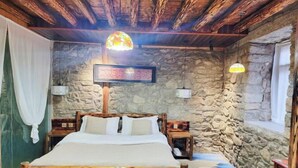 A rustic bedroom with a stone wall, wooden bed frame, two bedside tables, a large bed, and a hanging light fixture. - Zuji Youth Hostel (Dali City)