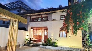 A courtyard with a traditional wooden door, a thatched roof structure, and a climbing plant with red flowers. - Zuji Youth Hostel (Dali City)