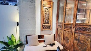 A wooden cabinet with intricate carvings, a cushioned bench with pillows, a camera, and a book on a small round table. - Zuji Youth Hostel (Dali City)