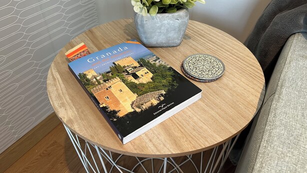 A book titled 'Granada and the Alhambra' on a round wooden table, a potted plant, and a decorative plate. - Charming 2-bedroom apartment with AC, WiFi in lovely Granada (Granada)