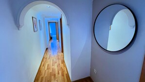 A hallway with wooden flooring, a round mirror on the wall, and a door leading to another room. - Charming 2-bedroom apartment with AC, WiFi in lovely Granada (Granada)