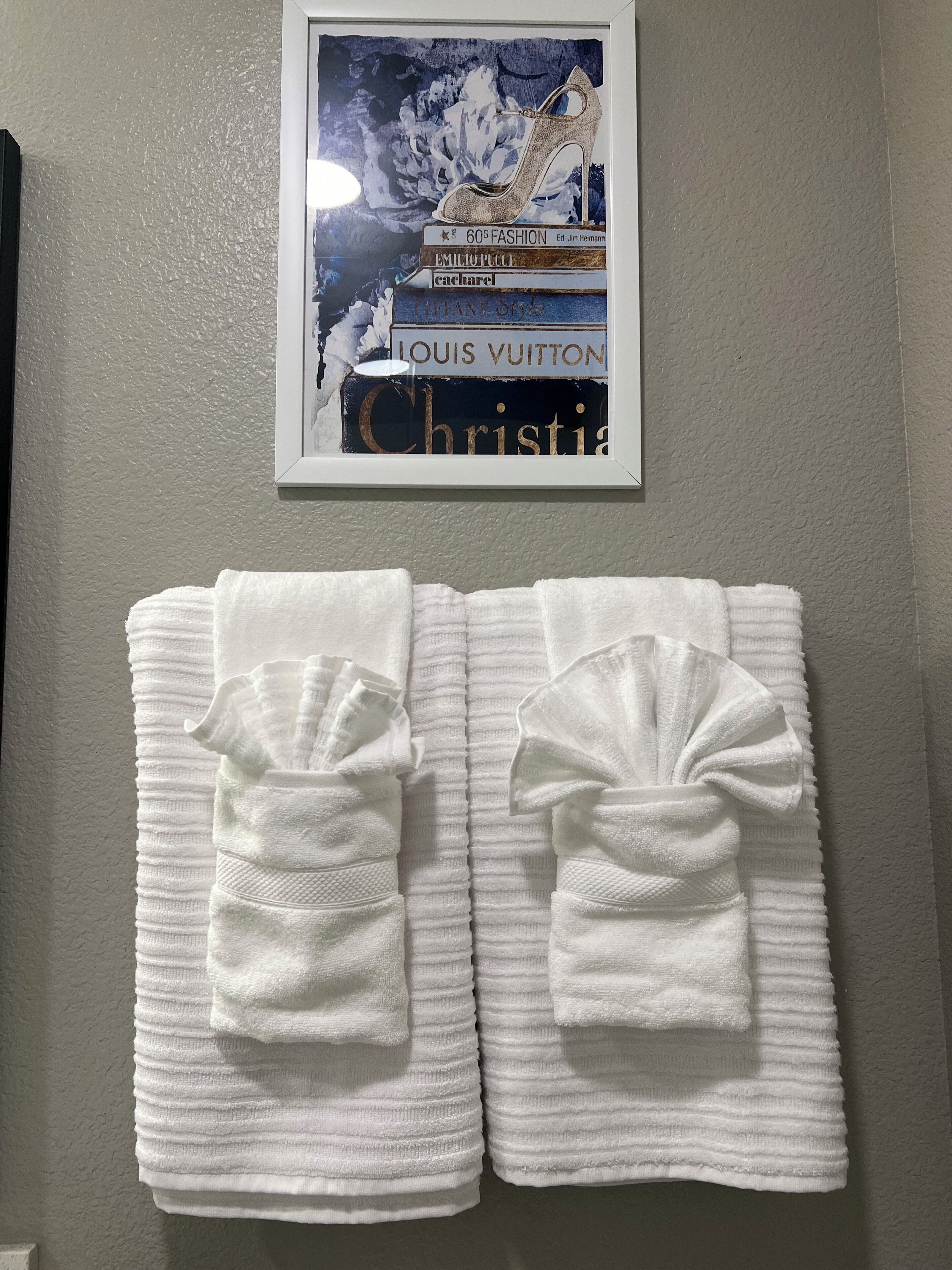 Une affiche encadrée représentant des marques de haute couture, accrochée à un mur, avec deux serviettes blanches pliées en dessous.