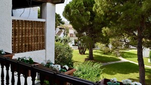 Een balkon met uitzicht op een verzorgde tuin, een wit gebouw met een houten balkon, en een heldere lucht.