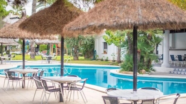 Een zwembadgedeelte met rieten parasols, ligbedden en tafels.
