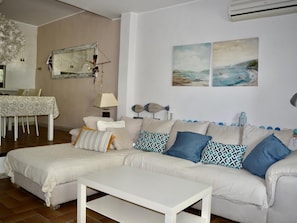 Una sala de estar con sofá, una mesa de centro, una mesa de comedor con sillas y decoración en la pared.