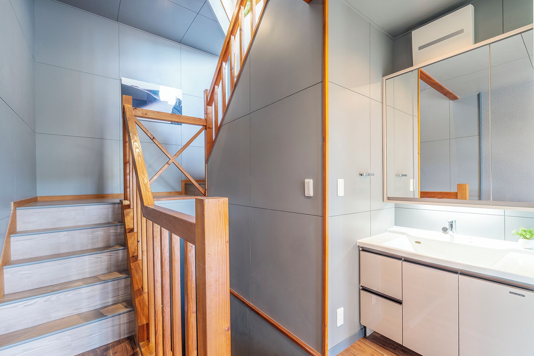 Un baño moderno con un espejo grande, un lavabo blanco y una escalera de madera.