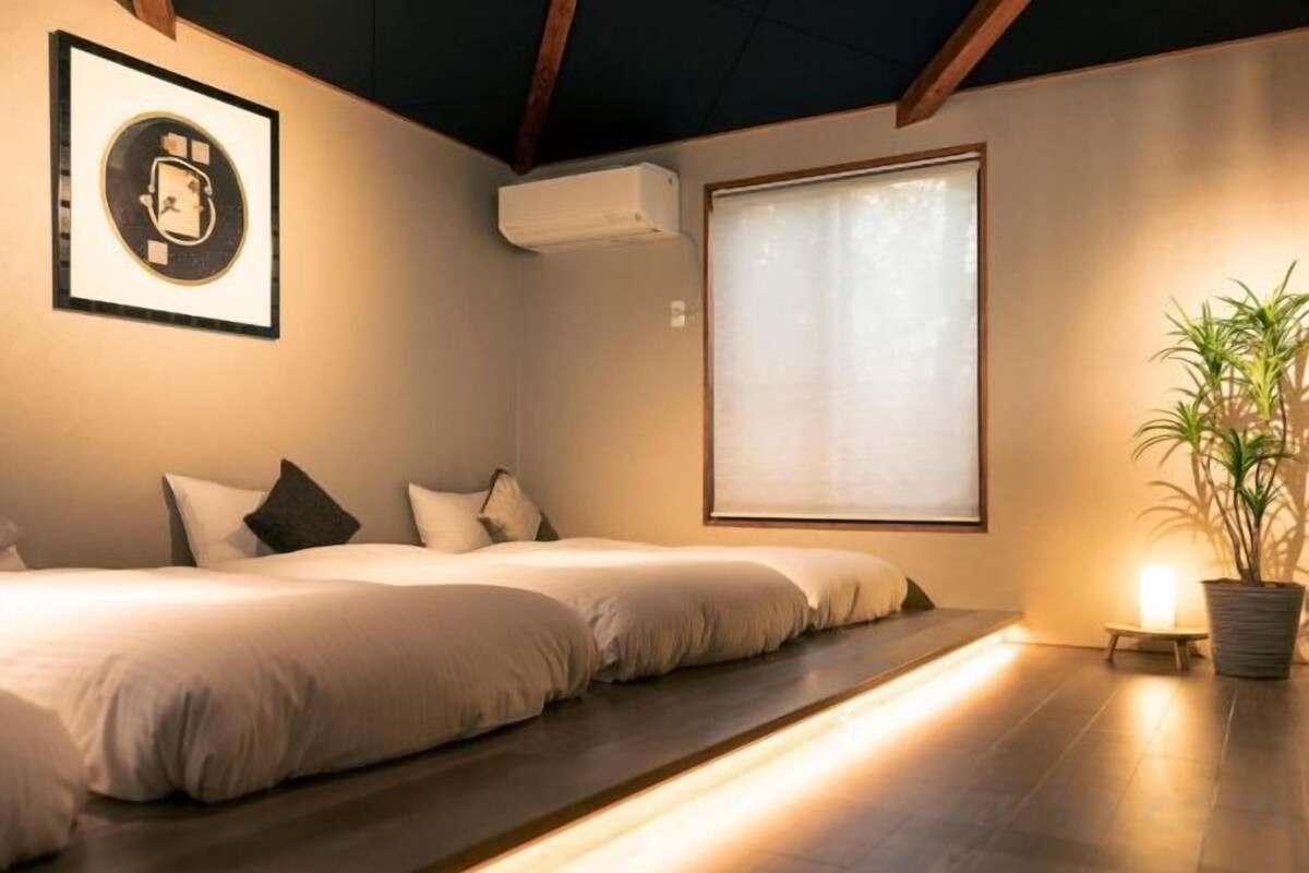 Une chambre avec deux lits, une grande fenêtre, un appareil de climatisation et une plante en pot.