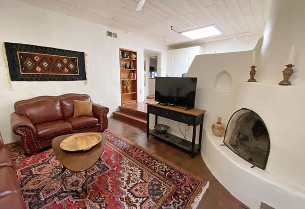 Una sala de estar con un sofá de cuero marrón, una mesa de centro, un televisor sobre un mueble bajo, una chimenea y una alfombra estampada.