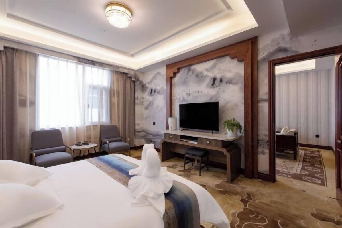 A hotel room with a large bed, a flat-screen TV, a desk with a chair, and a seating area with two armchairs.