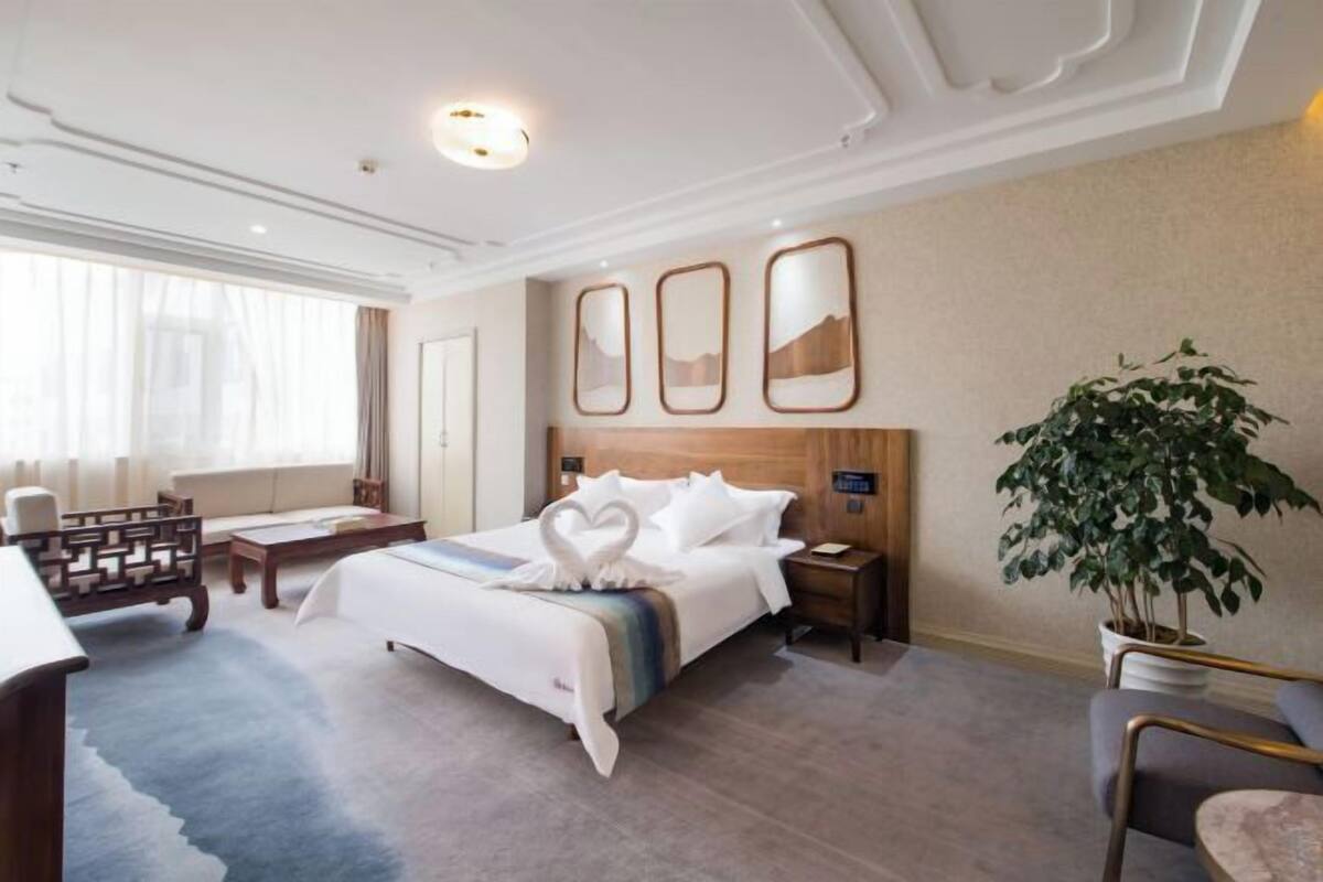 A hotel room with a large bed, a desk, a chair, and a potted plant.