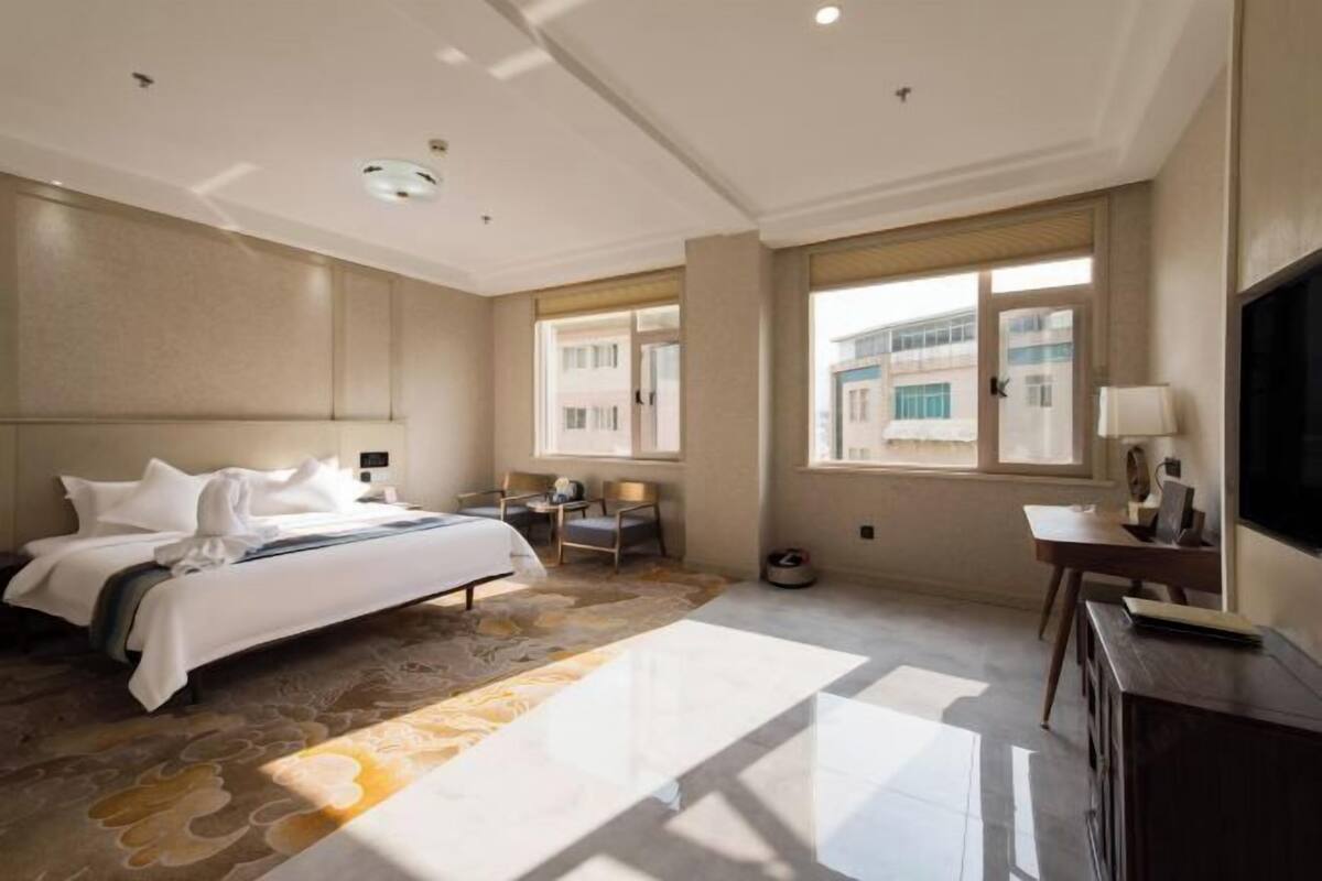 A hotel room with a bed, a desk, a chair, a TV, and large windows.