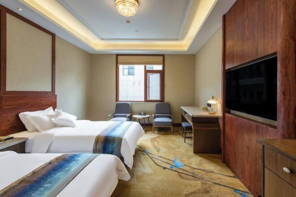 A hotel room with two beds, a desk, a TV, and a window.
