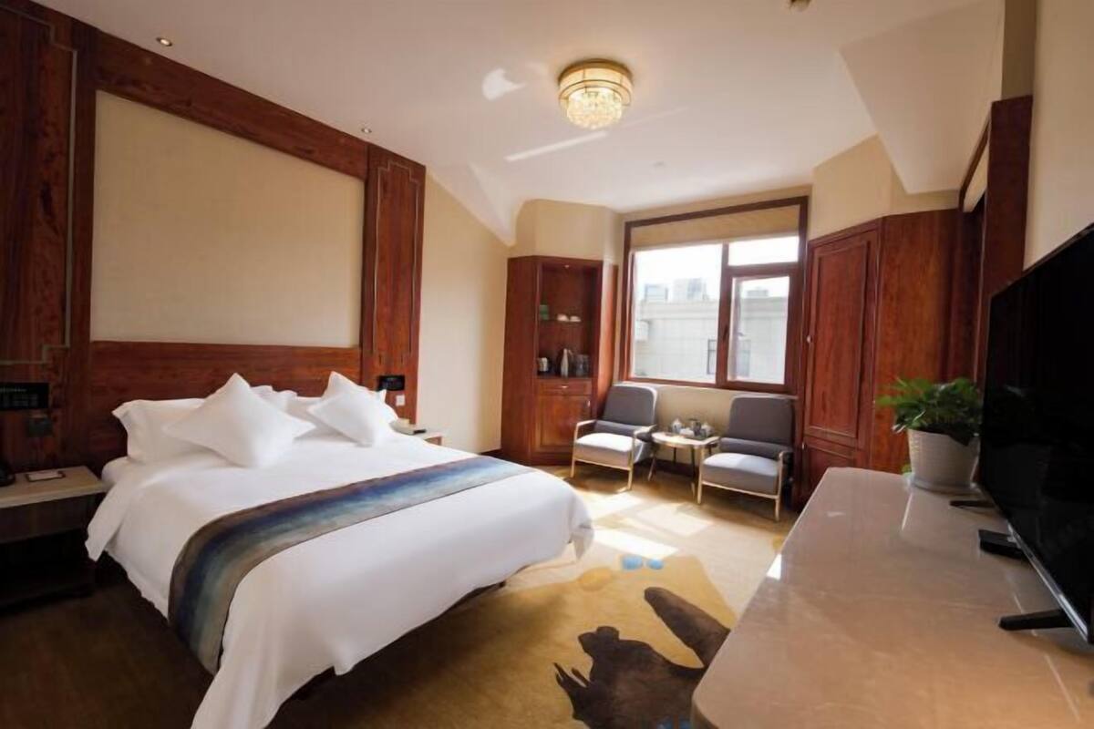 A hotel room with a large bed, a desk, a television, and a window with a city view.