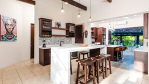 A modern kitchen with a central island, bar stools, pendant lighting, and a view of the outdoors. - Golf from home! 8BR Lux Villa, Pool, Beach Club! (Pinilla)
