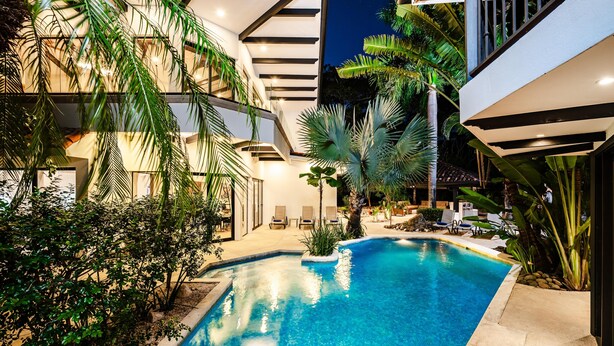A modern pool area with a clear blue pool, surrounded by lush greenery and palm trees. - Golf from home! 8BR Lux Villa, Pool, Beach Club! (Pinilla)