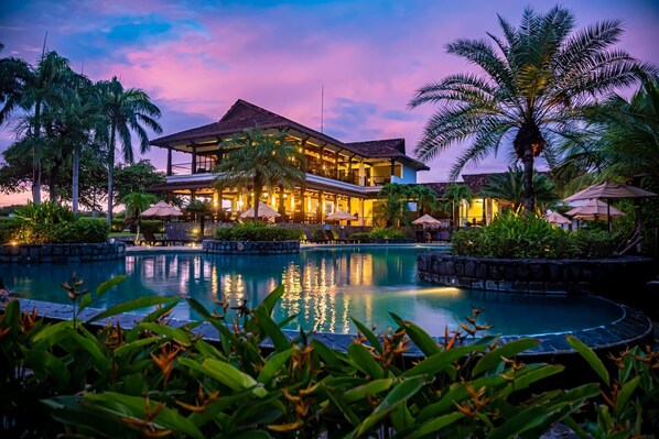A resort with a swimming pool, palm trees, and a building with multiple balconies.