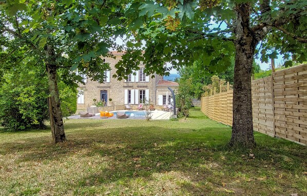 A stone building with a swimming pool, surrounded by a wooden fence and trees.