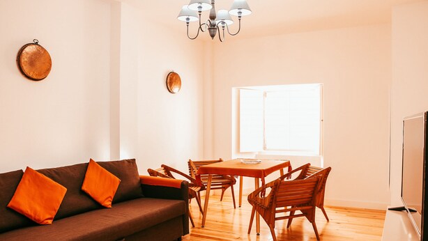 A living room with a sofa, wooden chairs, a dining table, and a TV. - Kalathos House 2 (Lisbon)