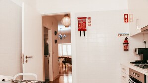A kitchen with white tiles, a dining area with a patterned table, and a hallway leading to a dining room. - Kalathos House 2 (Lisbon)