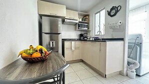 Eine kompakte Küche mit Kühlschrank, Mikrowelle und Spüle. Auf der Arbeitsplatte steht eine Obstschale, und ein Fenster sorgt für natürliches Licht.