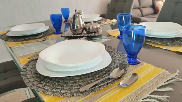 Ein Esstisch mit Geschirr, blauem Glas und Besteck auf einer gelb-schwarzen Tischmatte.