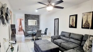 Ein modernes Wohnzimmer mit einem grauen Sofa, einem Esstisch mit Stühlen, einem Deckenventilator und gerahmten Bildern von Paris.