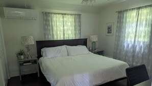 A neatly arranged bedroom with a bed, bedside tables, a lamp, a clock, and a framed picture on the wall.