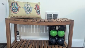 A wooden bench with a cushion featuring a hand and eye design, a spray bottle, and two green kettles.
