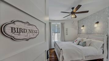 A bedroom with a bed, a ceiling fan, a wall-mounted sign reading "BIRD NEST", and a window with curtains.