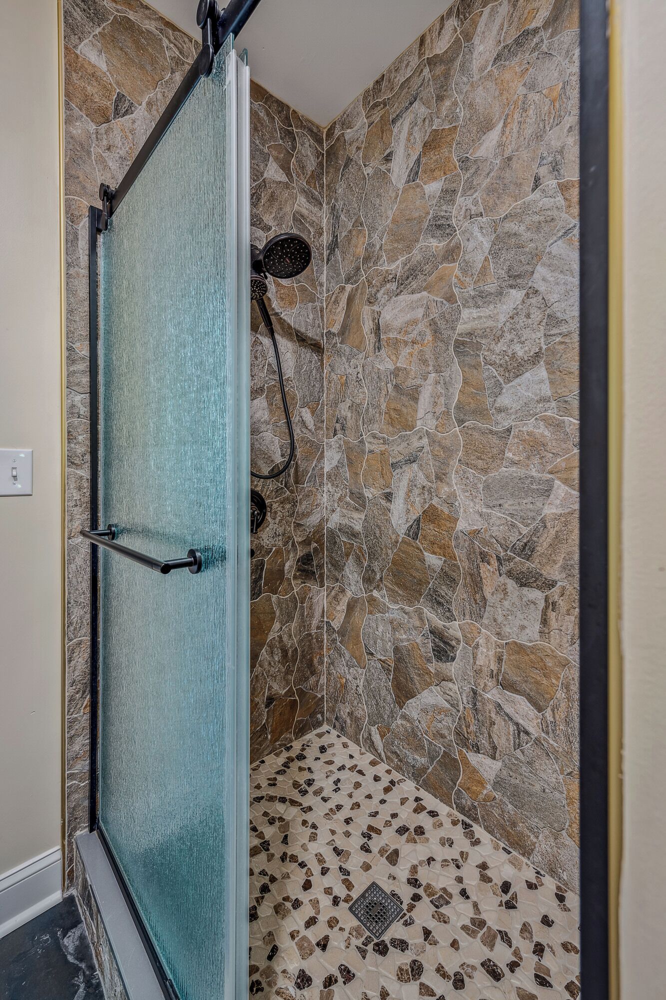 A shower with a glass door, stone walls, and a tiled floor.