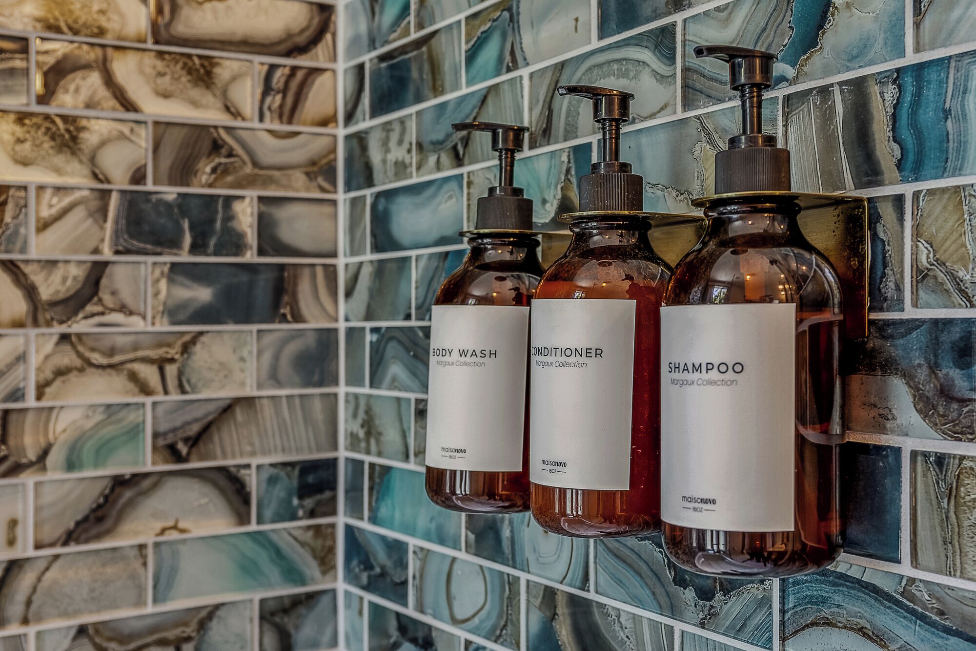 Et badeværelse med marmorbeklædt backsplash og tre flasker sæbe, balsam og shampoo.