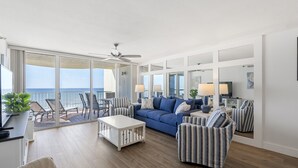 A spacious living room with a blue sofa, striped armchairs, a coffee table, and a balcony with a view of the ocean. - STEPS TO THE BEACH!!! Beautifully Renovated Unit w/Breathtaking Views (Miramar Beach)