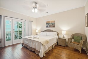 A bedroom with a large bed, a wicker chair, a nightstand, and a view through a sliding glass door.