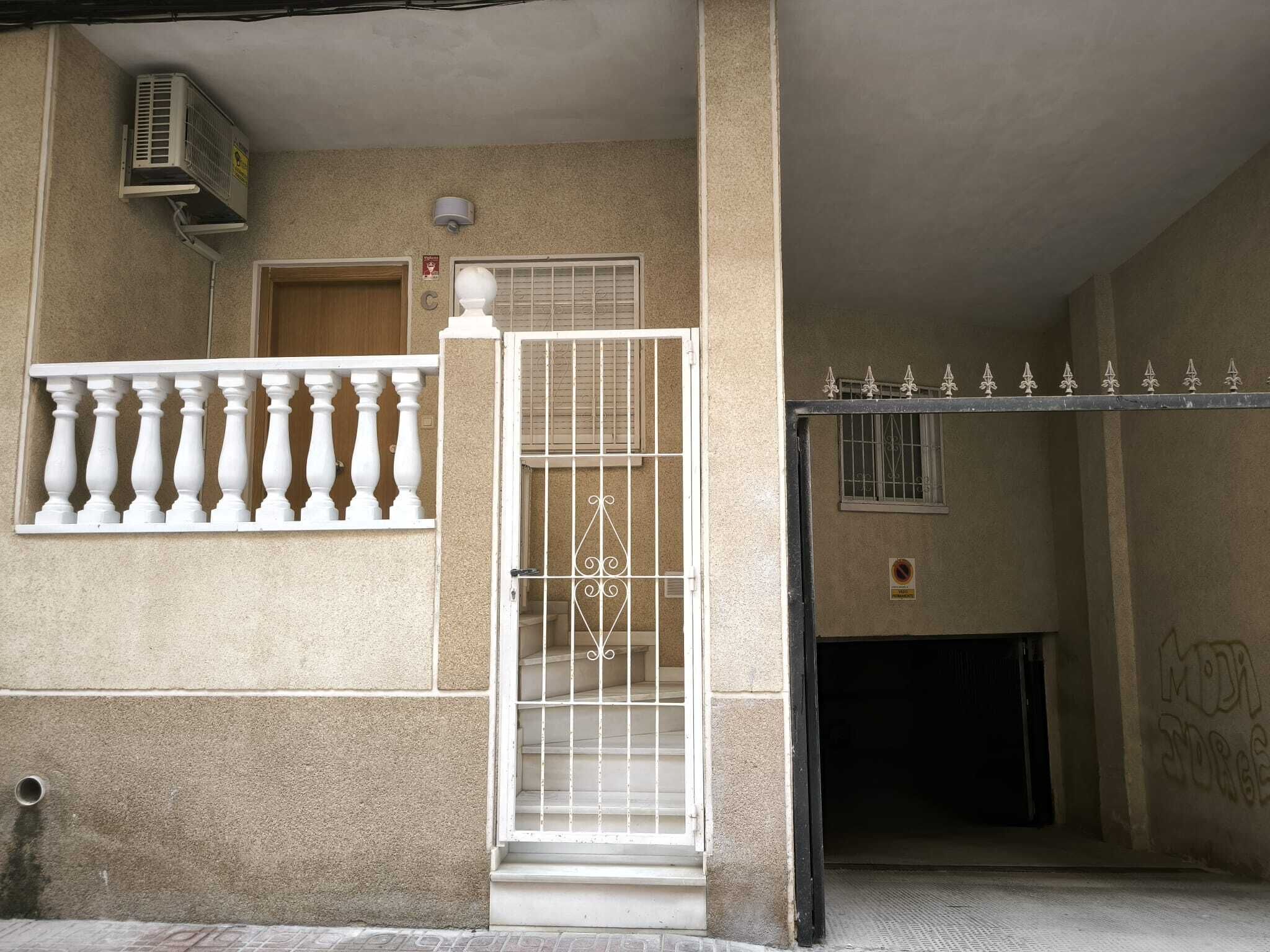A building entrance with a gated door, a small window, and a wall-mounted air conditioning unit.
