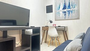 En stue med fjernsyn, skrivebord, stol og sofa.