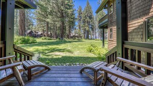 A wooden deck with benches, overlooking a grassy yard with trees and a building in the background. - Chambers Lakeside Retreat - Walk to Lake, Views & HOA Gym, Pool + Beach (Homewood)