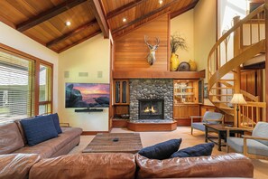 A spacious living room with a stone fireplace, leather sofas, a television, and a wooden staircase.