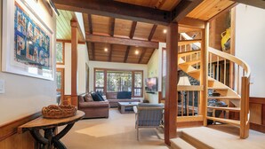 A spacious living area with a wooden staircase, a sofa, a coffee table, and a wicker basket. - Chambers Lakeside Retreat - Walk to Lake, Views & HOA Gym, Pool + Beach (Homewood)