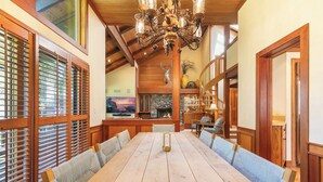 A spacious dining area with a long wooden table, cushioned benches, a chandelier, and a stone fireplace. - Chambers Lakeside Retreat - Walk to Lake, Views & HOA Gym, Pool + Beach (Homewood)