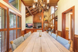 Een ruime eetruimte met een lange houten tafel, comfortabele banken, een kroonluchter en een stenen openhaard.