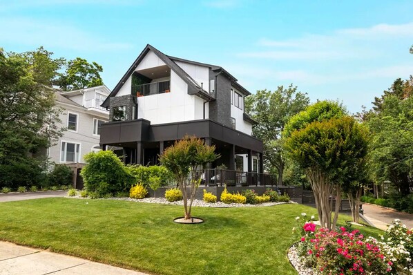 Une maison moderne à deux étages, à l’extérieur noir et blanc, entourée d’une pelouse bien entretenue et de plantes en fleurs.