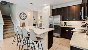Una cocina moderna con armarios de madera oscura, un refrigerador de acero inoxidable y una isla central con taburetes de bar.