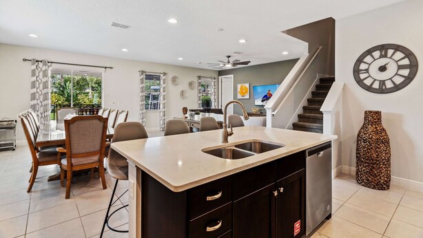 Una cocina moderna con una isla central, un comedor con mesa y sillas, y una escalera que sube a un nivel superior.