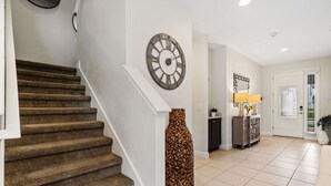 Una escalera con peldaños alfombrados, un reloj fijado a la pared, un jarrón decorativo, una lámpara y una puerta que da a otra habitación.
