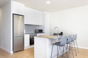 A modern kitchen with white cabinetry, stainless steel appliances, and a central island with bar stools. - Home2Book Nordés Apartment Pool & Terrace, Abades (Abades)
