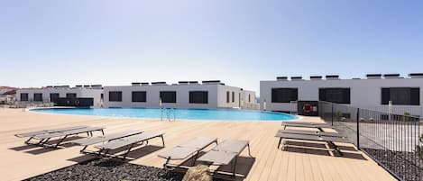 Un área de piscina con sillones de descanso y un edificio con amplias ventanas.
