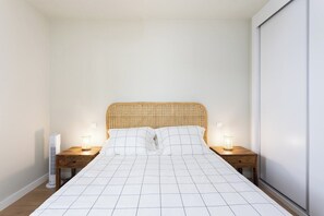 A bedroom with a bed, two bedside tables, a nightstand, a wall-mounted heater, and a sliding door. - Home2Book Nordés Apartment Pool & Terrace, Abades (Abades)